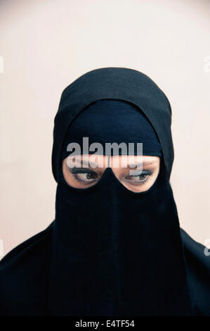 Portrait of young woman in black, muslim hijab and muslim dress, eyes looking to the side with eye makeup, on white background