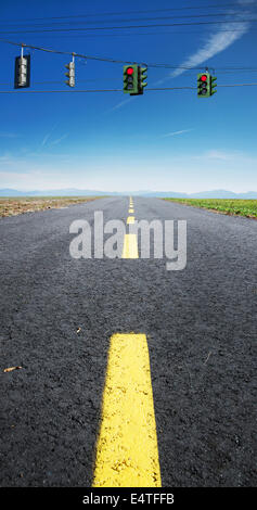 Close-up view of yellow, broken center line on deserted highway, with red traffic lights hanging on wires across road, Canada Stock Photo