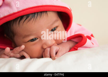 Close-up portrait of two week old Asian baby girl in pink polka dot hooded jacket, studio shot Stock Photo