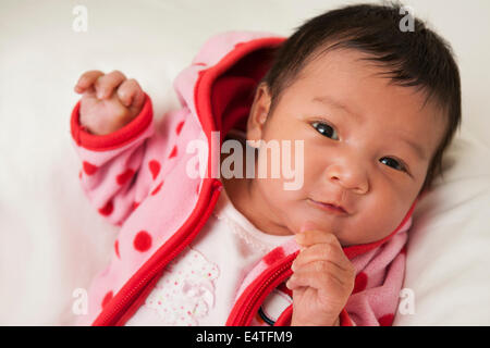 Close-up portrait of two week old Asian baby girl in pink polka dot jacket, smiling and looking at camera, studio shot Stock Photo