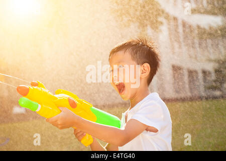 little boy shouting and playing water guns in the park Stock Photo