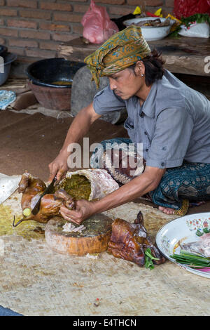 Bali, Indonesia.  Roasted Pig Being Cut up by Village Cook.  He is wearing the udeng, the traditional Balinese head cloth. Stock Photo