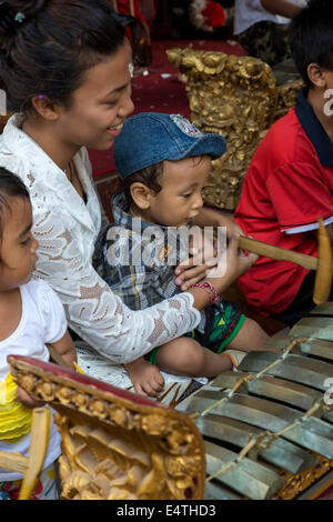 Bali, Indonesia.  Balinese Hindu Mother Showing Child how to Hit a Xylophone with its Wooden Hammer. Stock Photo