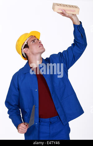 young bricklayer in jumpsuit inspecting brick Stock Photo