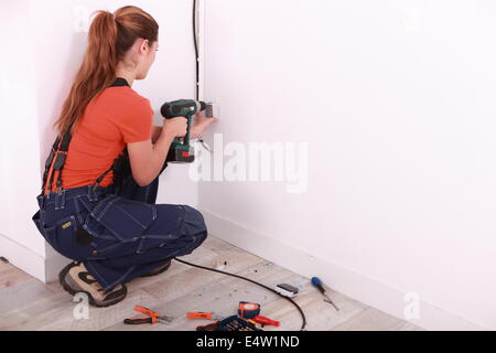 Woman drilling hole in wall Stock Photo