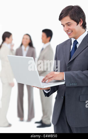 Smiling salesman with his laptop and associates behind him Stock Photo ...