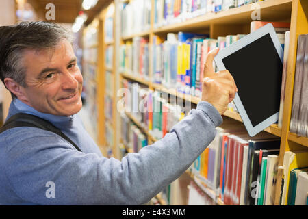 Smiling man taking a tablet pc from shelves Stock Photo