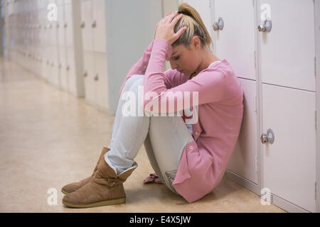 Upset student sitting on floor of hallway Stock Photo