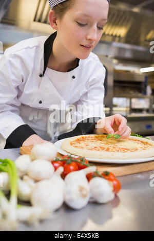 Chef putting basil leaf on pizza Stock Photo