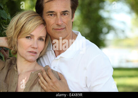 Sultry couple stood by tree in park Stock Photo