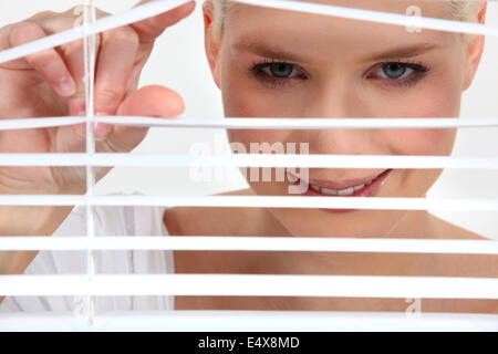 Woman peering through blinds Stock Photo
