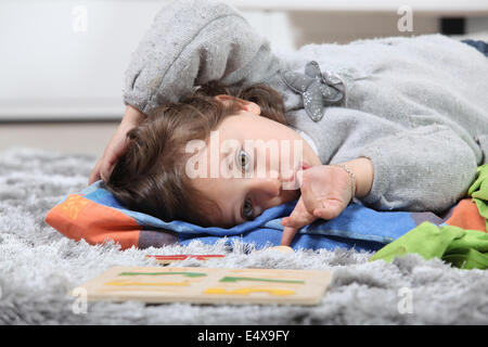 Little girl laying on rug next to puzzle Stock Photo