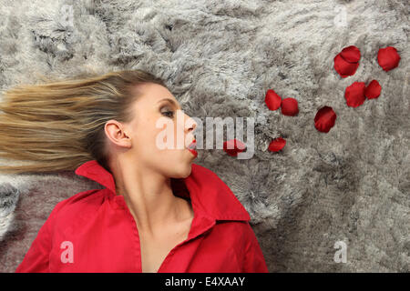 blonde in red blowing away red rose petals Stock Photo