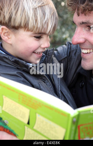 Man with little boy reading book outdoors Stock Photo