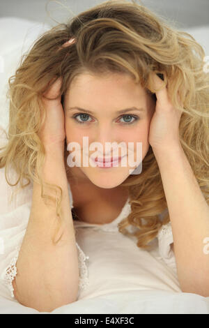 a blonde woman on a bed touching her hair Stock Photo