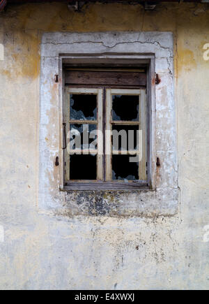 Broken glass in a window with wooden frames with decaying plaster on surrounding wall Stock Photo