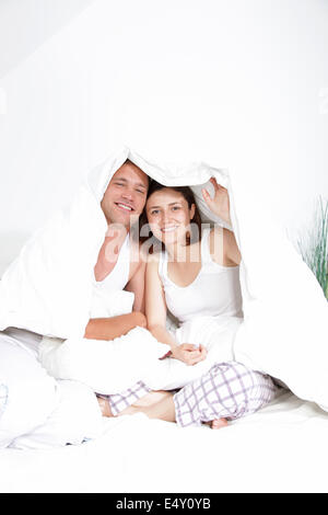 Smiling young couple sitting under the duvet Stock Photo