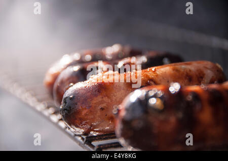 Sausages cooking on a bbq grill, sizzling and smoking away in the sunshine Stock Photo