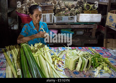 Bali, Indonesia.  Woman Making Offering Baskets  (Canang) from Palm Fronds in Jimbaran Market. Stock Photo