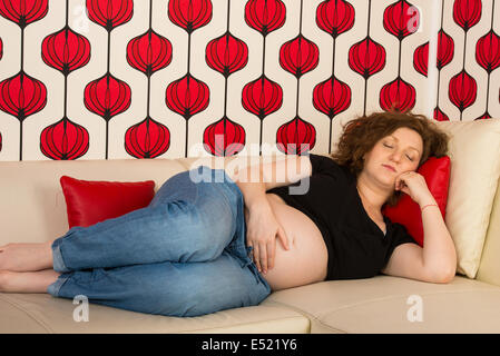 Sleeping pregnant woman on sofa in living room Stock Photo