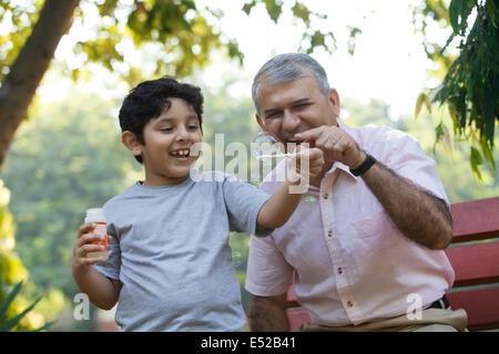 Boy blowing bubbles in a park while grandfather looks on Stock Photo