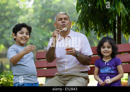 Grandfather blowing bubbles with grandchildren in park Stock Photo