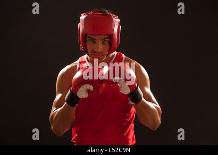 Portrait of an Indian boxer wearing gloves and head protector over black background