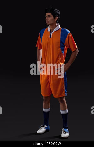 Soccer player standing with hands on hip as he looks away isolated over black background Stock Photo
