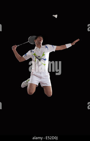 Young male player jumping to hit shuttlecock with racket over black background Stock Photo