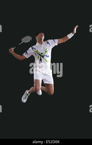 Young male player holding badminton racket while jumping in mid-air Stock Photo