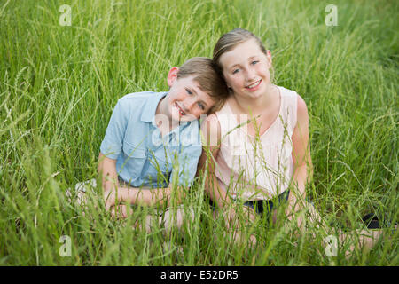 Brother and sister sitting side by side, in long grass. Stock Photo