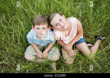 Brother and sister sitting side by side, in long grass. Stock Photo