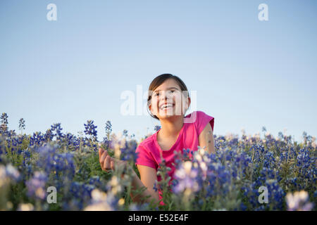 A young girl sitting in a field of wild flowers, laughing. Stock Photo