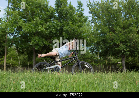 A young boy falling off his bicycle, overbalancing in a grassy field. Stock Photo