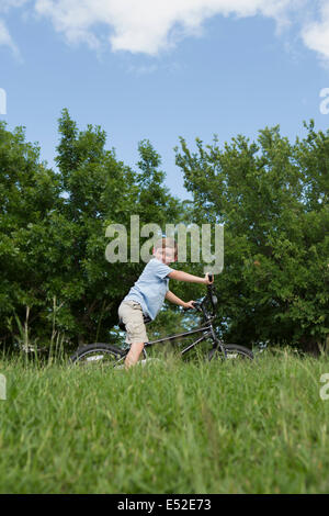 A young boy riding a bicycle through grass in a meadow. Stock Photo