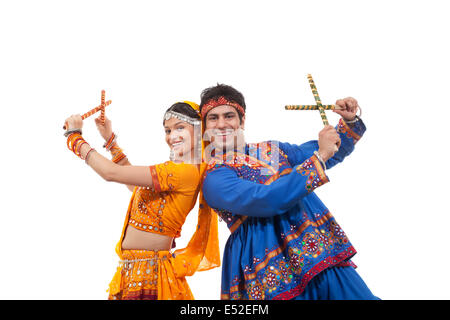 Portrait of happy young couple in traditional wear standing back to back while performing Dandiya Raas over white background Stock Photo