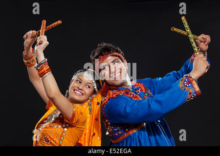 Young Indian couple in traditional wear performing Dandiya Raas against black background Stock Photo