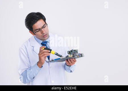 Young male technician repairing circuit board against gray background Stock Photo