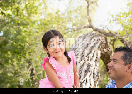 A young girl sitting on a tree trunk beside her father. Stock Photo