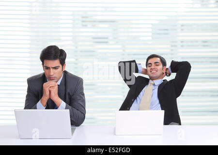 Worried businessman using laptop with colleague relaxing at desk in office Stock Photo