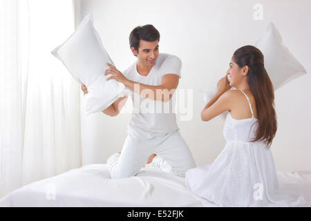 Playful young couple having pillow fight on bed Stock Photo