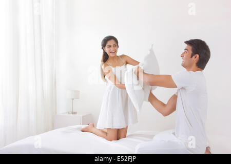 Excited young couple having pillow fight on bed Stock Photo
