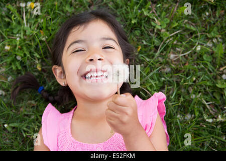 A girl lying on the ground, holding a dandelion seedhead clock. Stock Photo