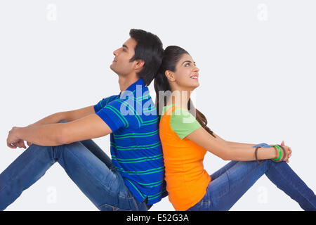 Side view of thoughtful young couple sitting back to back on white background Stock Photo