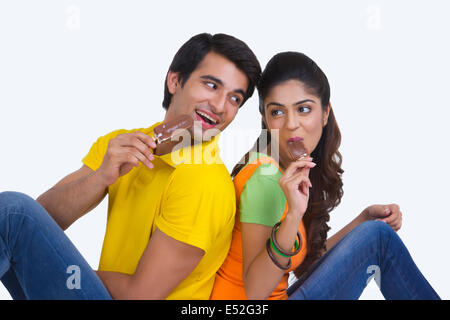 Young Indian couple eating chocolate ice-cream bars over white background Stock Photo
