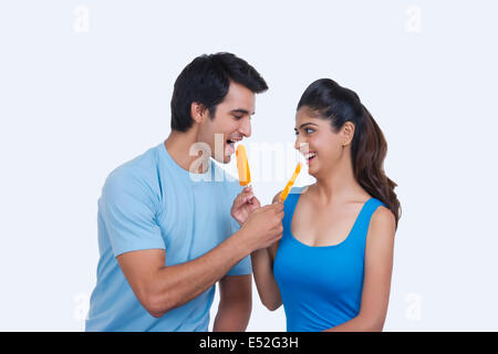 Loving young couple feeding each other ice lollies over white background Stock Photo