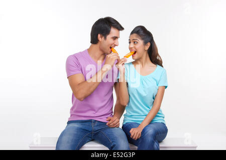 Loving young couple eating ice lollies on bench isolated over white background Stock Photo