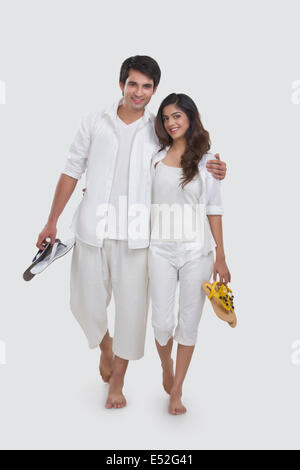 Portrait of loving young couple holding slippers while walking over white background Stock Photo