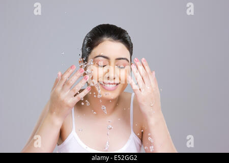 Beautiful woman splashing water on face against gray background Stock Photo