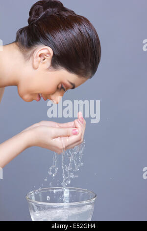 Profile shot of young woman washing face with water over blue background Stock Photo